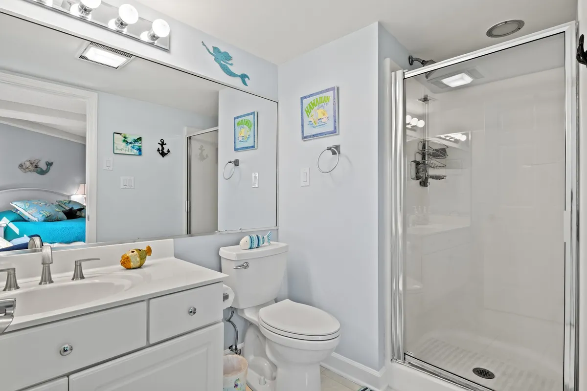 A bright bathroom with a sleek vanity and mirror, a spacious shower area, and cheerful decorative artwork. The space offers both functionality and a refreshing atmosphere, ideal for morning routines or relaxing showers.