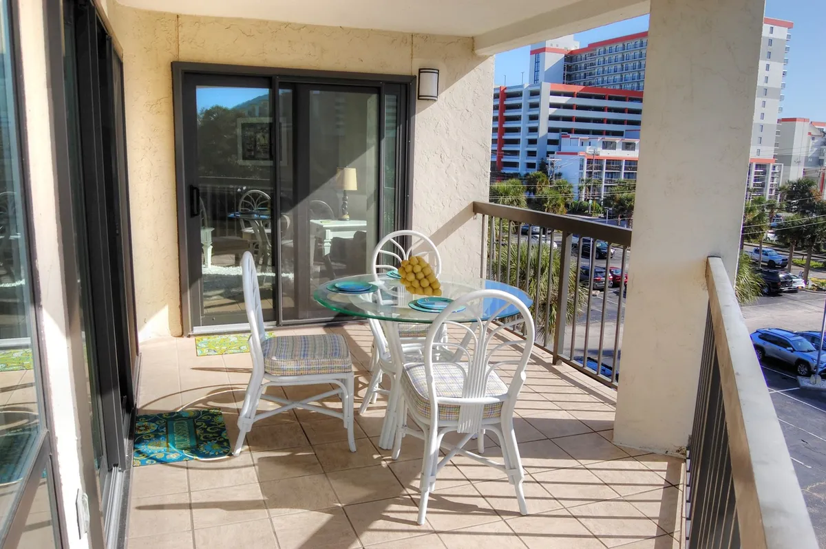 A tranquil balcony setting with a glass table and white chairs, offering a relaxing spot to enjoy morning coffee or evening conversations while overlooking the pool or gardens.