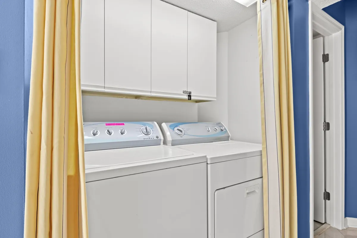 A laundry area featuring a washing machine, dryer, storage cabinets, and decorative curtains. The layout is functional and tidy, hinting at the convenience of in-unit laundry for longer stays or family trips.